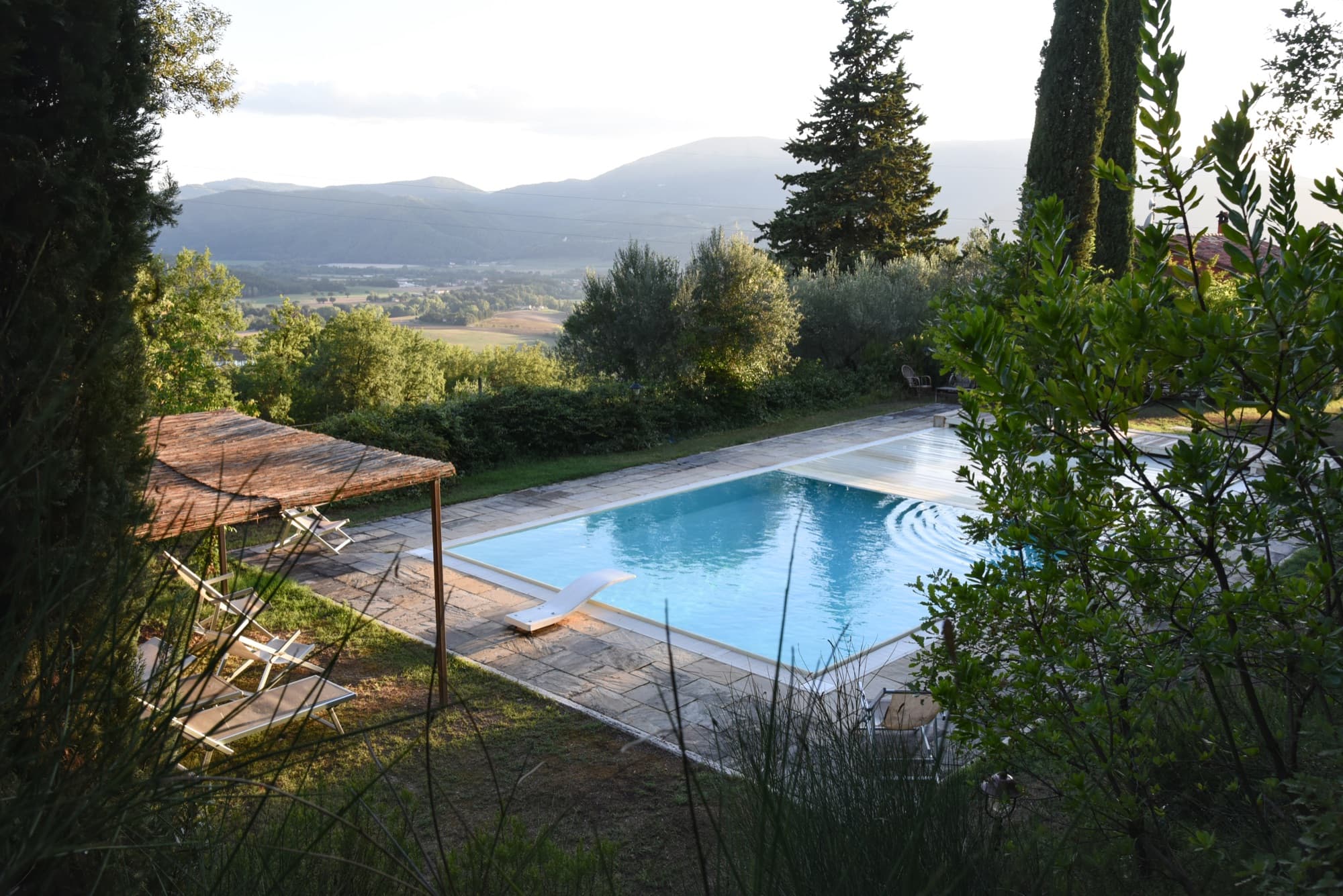 La piscina tra gli alberi, con la pergola, i lettini e la valle sullo sfondo