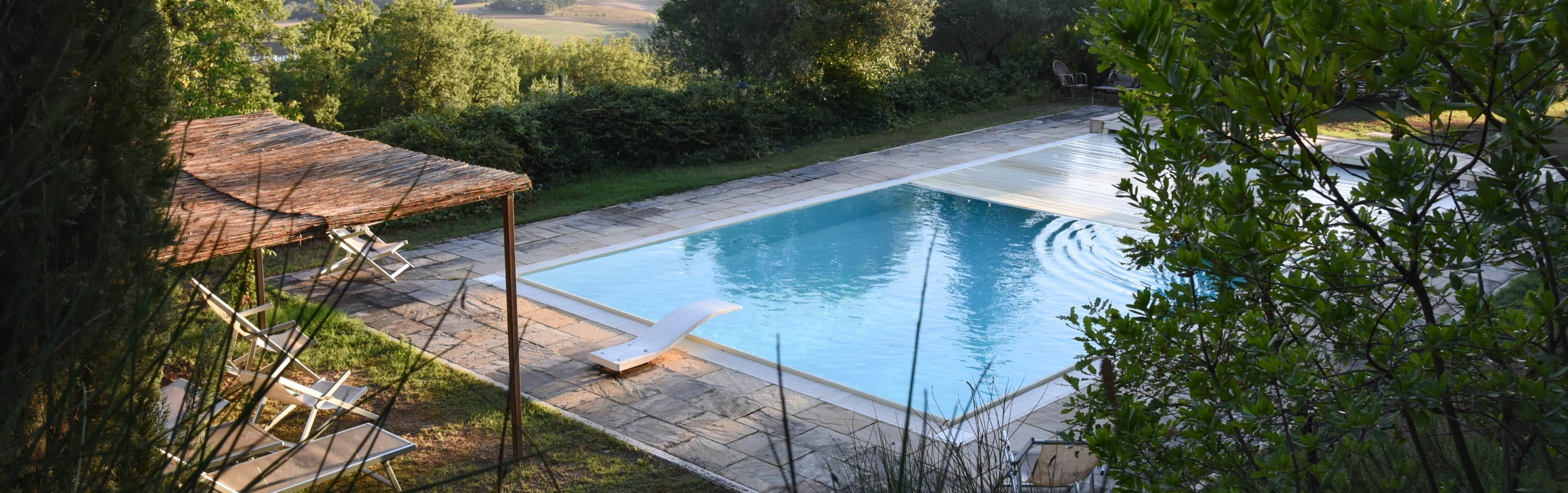 La piscina vista dall’alto tra gli alberi, con la pergola e i lettini