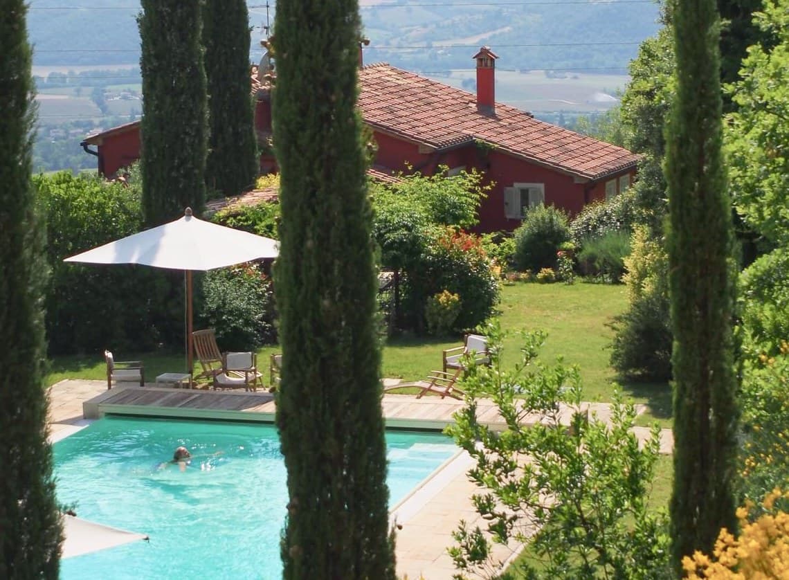 La casa e la piscina viste tra i cipressi, con le montagne sullo sfondo